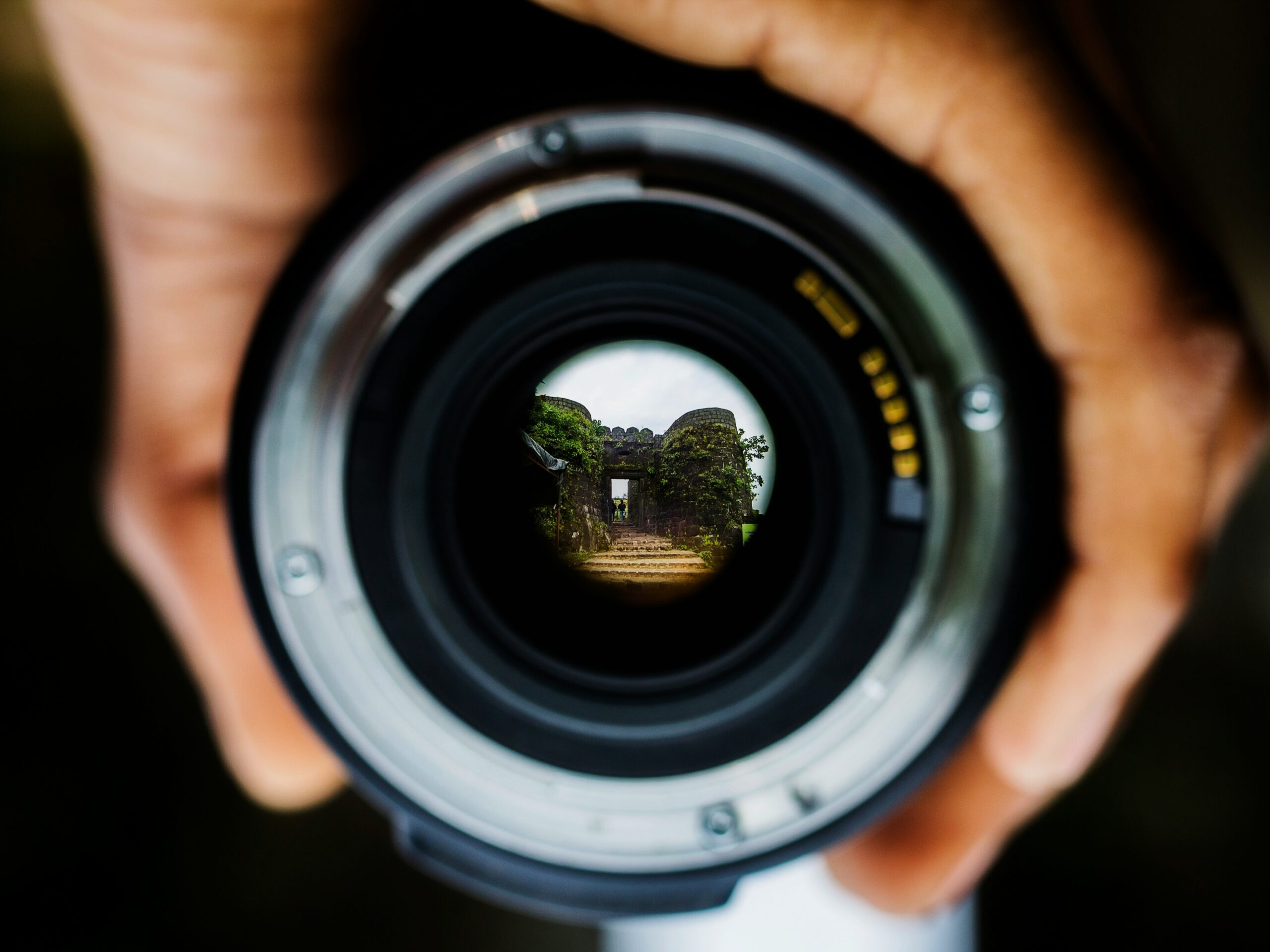 Hand holding a camera lens with a view of the world through it, symbolizing the exploration and discovery of travel on Life Through Us.