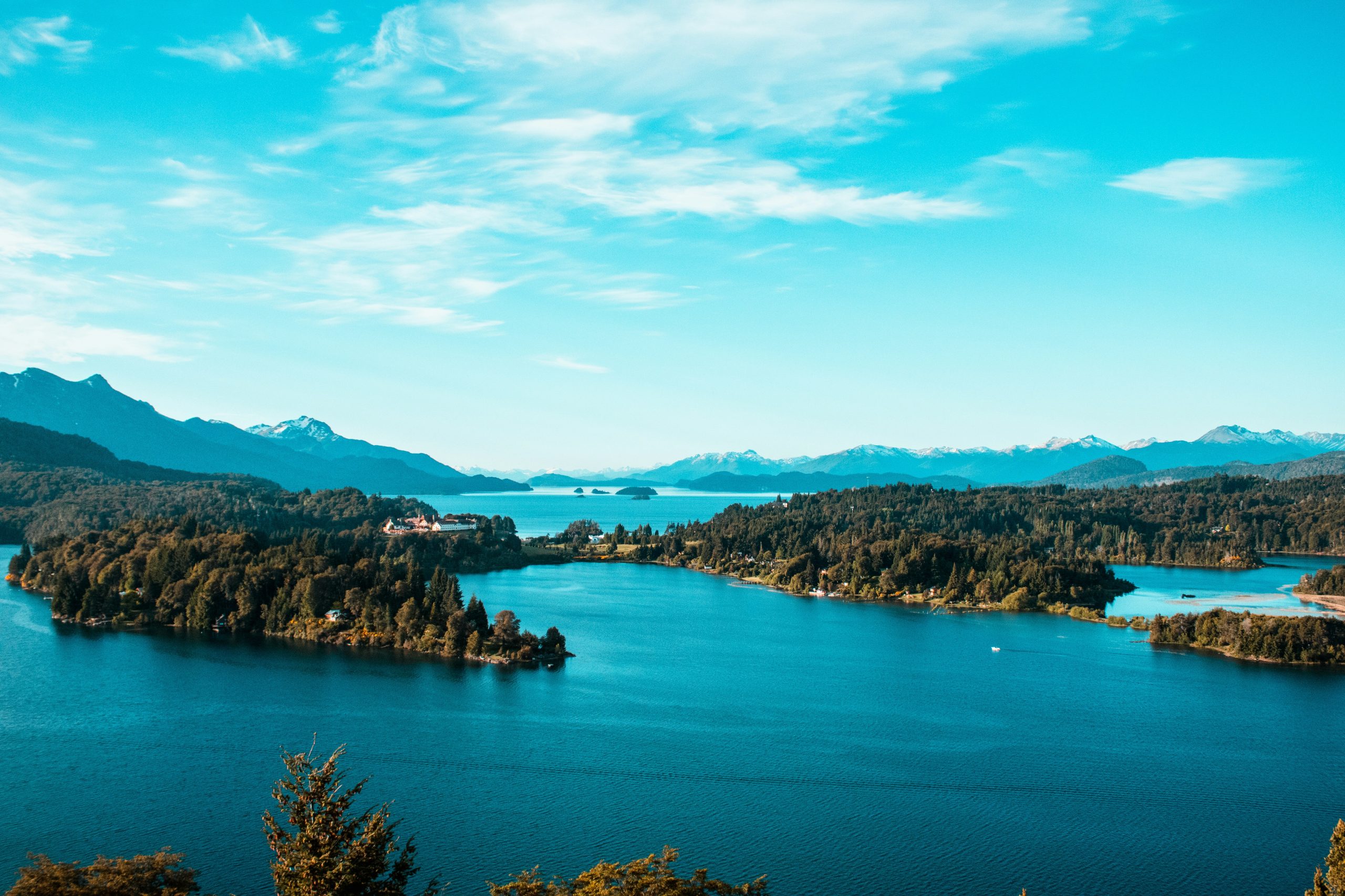 Panoramic view of Nahuel Huapi Lake in Bariloche, Argentina, with clear blue waters, lush green islands, and distant snow-capped mountains.