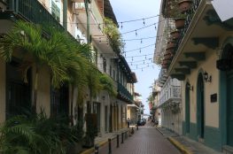 Cobblestone street in Casco Viejo, Panama, flanked by colonial buildings with balconies and lush green plants.