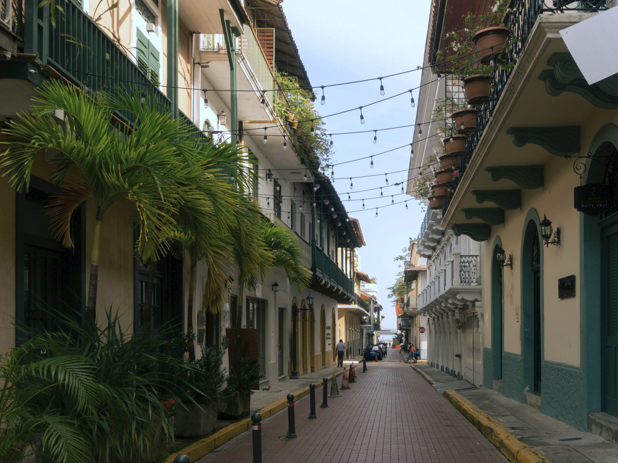 Cobblestone street in Casco Viejo, Panama, flanked by colonial buildings with balconies and lush green plants.